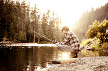 Young Man Fishing In Lake At Sunset