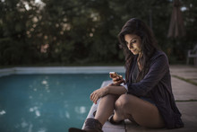 Woman Using Mobile Phone While Sitting At Poolside During Sunset