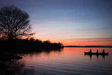 Silhouetted Women Rowing Boat In Lake Against Sky During Sunset