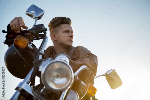 Low angle view of man sitting on motorcycle against clear sky Poster