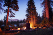 © Cavan Images - Woman sitting near fire at camp at dusk