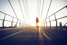 Man Cycling Along Bridge At Sunset