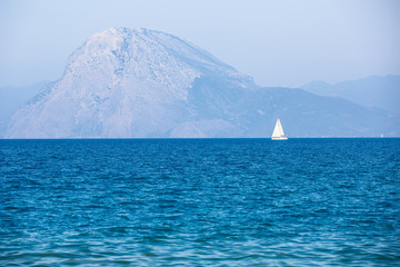 White sailboat in the blue sea with mountains