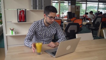 Poster - Businessman working in the office. In the big room of creative agency people have business meeting. Male concentrated at his work. Guy looking on the laptop and surfing internet.He is drinking orange