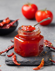 Tomato and chili sauce, jam, confiture in a glass jar on a grey stone background