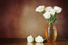 Still Life With White Roses In The Vase On A Wooden Surface Against Brown Background