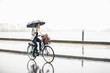 © Maskot - Full length of businesswoman riding bicycle on wet city street during rainy season