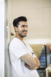© Maskot - Smiling young male doctor leaning on wall in hospital