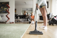 Low Section Of Girl Cleaning Floor With Vacuum Cleaner At Home