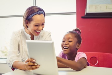 Teacher and school girl using digital tablet in classroom