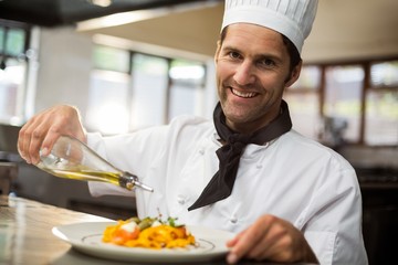 Wall Mural - Portrait of happy chef pouring olive oil on meal