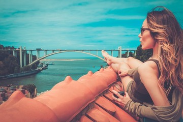 Woman enjoying sunbath with glass of port wine on the rooftop, on river bridge background.