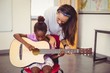 © WavebreakMediaMicro - Teacher assisting a girl to play a guitar in classroom