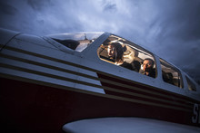 Low Angle View Of Mid Adult Man Flying Aeroplane With Friend Sitting Behind At Dusk