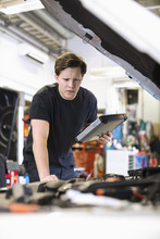 Serious Young Male Car Mechanic With Digital Tablet Analyzing Car Engine