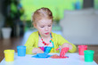 © cromary - Laughing little child, blonde artistic toddler girl painting and drawing with colorful finger paints indoors at bright room at home or kindergarten.