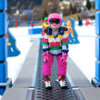 © cromary - Happy child enjoying winter vacation in Alpine resort in Austria. Active sportive toddler girl learning to ski. Kid having fun in ski school going up to the slope on the magic carpet lift.