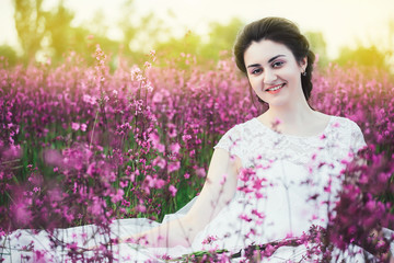 Wall Mural - beautiful bride in a flower field. The girl in a white dress with a bouquet in a summer field at sunset