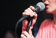 Microphone And Unrecognizable Female Singer Close Up. Cropped Image Of Female Singer In Pink Dress , Singing Into A Microphone, Holding Mic With Two Hands. Copyspace
