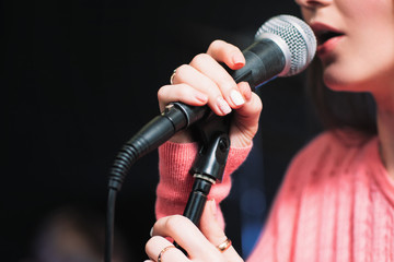 Microphone and unrecognizable female singer close up. Cropped image of female singer in pink dress , singing into a microphone, holding mic with two hands. Copyspace