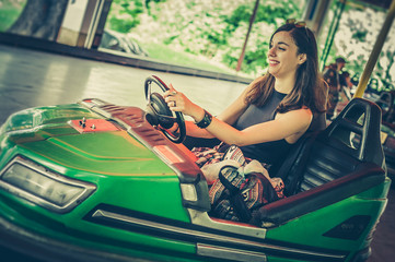 Wall Mural - Cute young woman having fun in electric bumper car in amusement park