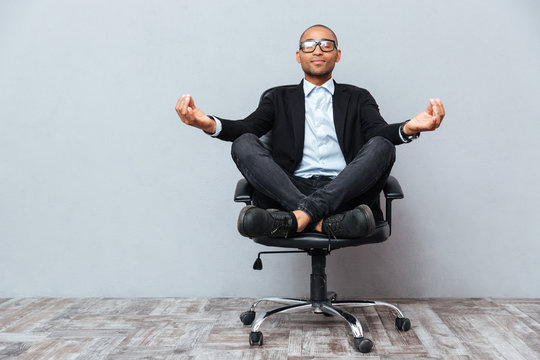 relaxed african young man sitting and meditating on office chair