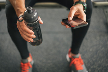 Fitness man looking to the phone for motivation before gym workout. Sporty male athlete looking his smartphone holding water bottle.