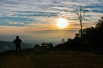 Silhouette of man is standing on top of mountain at sunrise.