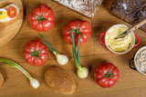 Fototapeta Kuchnia - Drewniany stół zastawiony pomidorami, cebulkami, chlebem i masłem, kompozycja