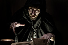 Necromancer Casts Spells From Thick Ancient Book By Candlelight On A Dark Background