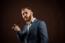 Portrait Of Handsome Confident Man In Suit Holding Smoking Pipe Against Of Brown Background.Isolated.