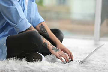 Poster - Young man with tattoo using laptop on a floor at home