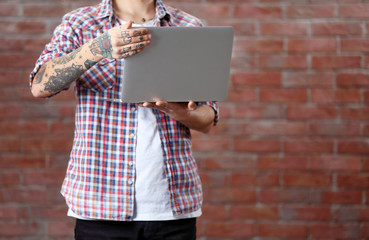 Poster - Young man with tattoo holding laptop on brick wall background