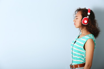 African American woman listening to music in headphones on grey background