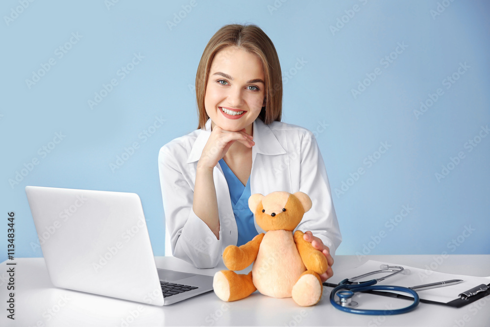Young beautiful female doctor at the table on wall background