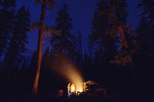 People Standing By Bonfire At Campsite In Forest During Night