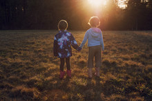 Rear View Of Sisters Holding Hands While Standing On Grassy Field