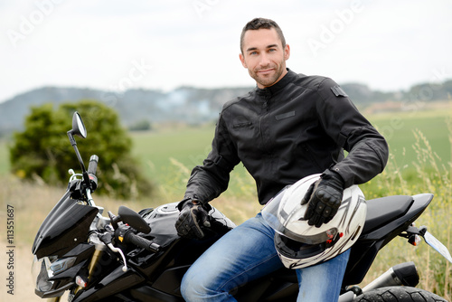Plakat przystojny młody mężczyzna rowerzysta z białym kasku jazda motocyklem czarny
