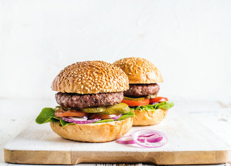 Fresh homemade burgers on wooden serving board with onion rings.