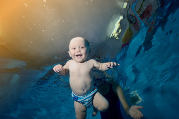 Wall Mural - Happy baby swims and plays under water in the pool on a blue background and laughs. Close-up. Horizontal orientation