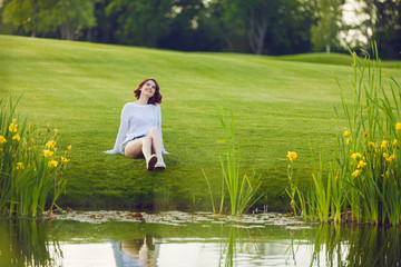 Wall Mural - Outdoor photo of young woman near the pond. Beautiful tender woman with red hair posing in summer park.