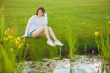 Wall Mural - Outdoor photo of young woman near the pond. Beautiful tender woman with red hair posing in summer park.