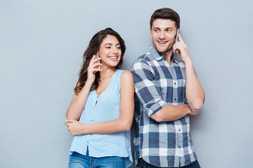 Canvas Print - Smiling couple using mobile phones over gray background