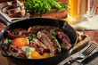 Male brutal dinner of fried sausages, bacon, scrambled eggs on the background of beer, herbs and bread