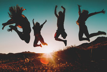 Four People Jumping Over The Sky At Sunset. Sunbeam In The Background.