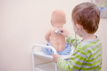 kid playing doctor with a stethoscope. boy playing with a doll and treats it. view from the back. copy space for your text