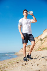 Poster - Sportsman standing and drinking water on the beach