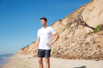 Poster - Thoughtful attractive young man standing on the beach and thinking