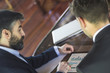 © GENETTICA - Young businessman with beard and some gray hairs pointing his finger on a tablet to show his co-worker information in graphical form. All screen graphics are made up.
