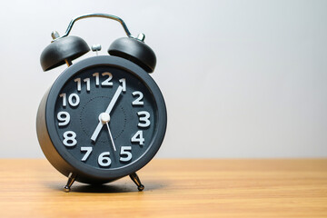 Wall Mural - Black alarm clock place on wood table in burred background